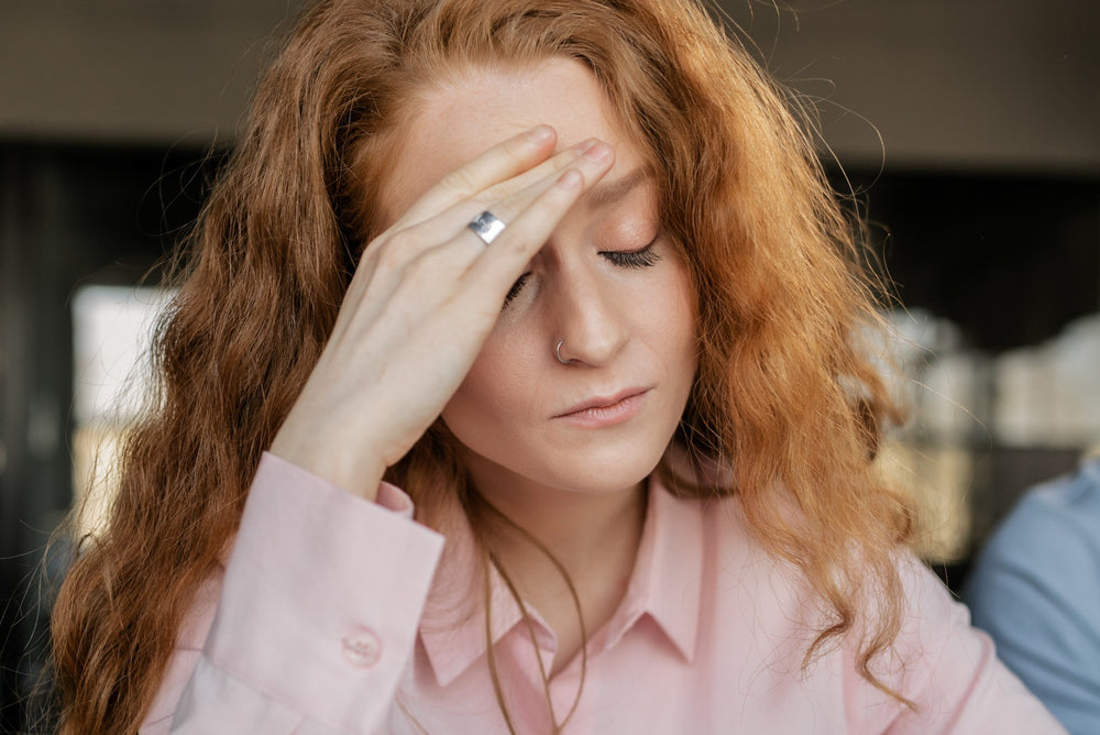 Redheaded woman looking at clipboard with her hand pressed to her forehead