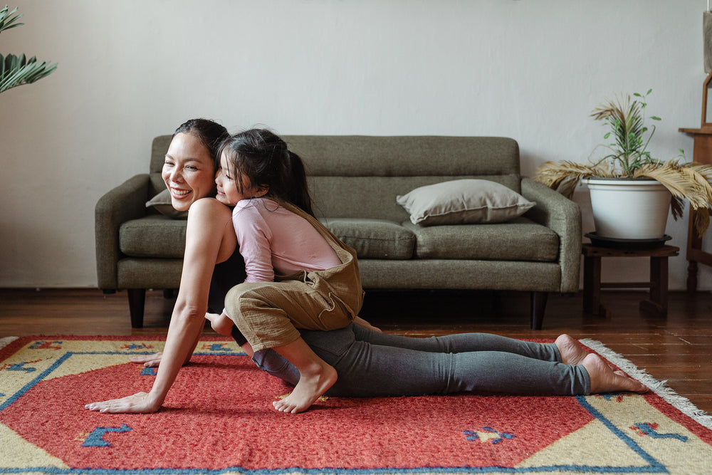 woman practicing yoga at home with her daughter playfully sitting on her